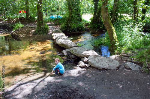 Senderismo en el Camino de Santiago. Un niño se refresca en la orilla de un rioi al lado de un puente hecho con piedras