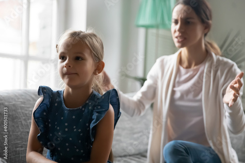 Close up angry strict mother scolding naughty daughter, sitting on couch at home, stubborn little girl ignoring parent, mum shouting at child, bad relationship, family generations conflict concept