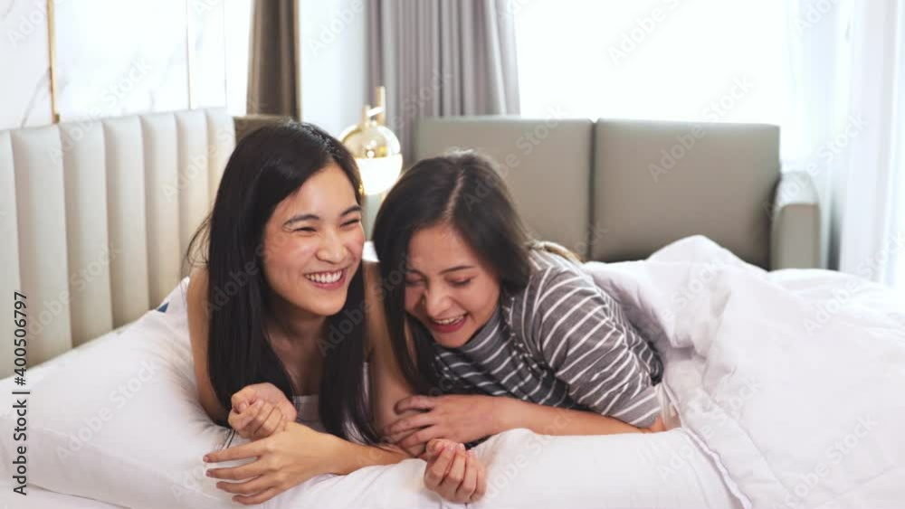 Homosexual mixed race lesbian couple lying on bed, looking each other. Two women sharing love and support holding hands. Gay family. LGBTQI, Pride Event, LGBT Pride Month, friendship concept. Homosexual mixed race lesbian couple lying on bed, looking each other. Two women sharing love and support holding hands. Gay family. LGBTQI, Pride Event, LGBT Pride Month, friendship concept.