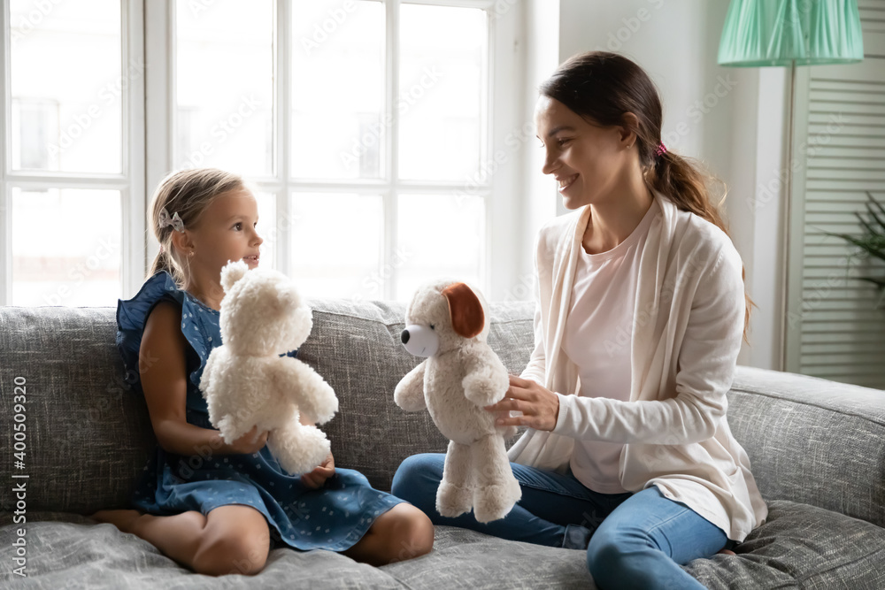 Close up happy young mother and little daughter playing with fluffy toys, sitting on cozy couch at home, smiling mum with adorable child girl having fun, family enjoying leisure time, weekend Close up happy young mother and little daughter playing with fluffy toys, sitting on cozy couch at home, smiling mum with adorable child girl having fun, family enjoying leisure time, weekend