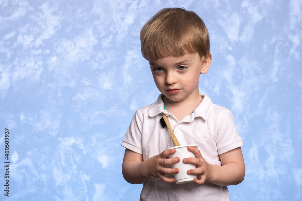 little boy holding a bamboo toothbrush and disposable cup of cornstarch in the bathroom on a blue texture background. ecologicaly clean. morning hygiene concept. little boy holding a bamboo toothbrush and disposable cup of cornstarch in the bathroom on a blue texture background. ecologicaly clean. morning hygiene concept.