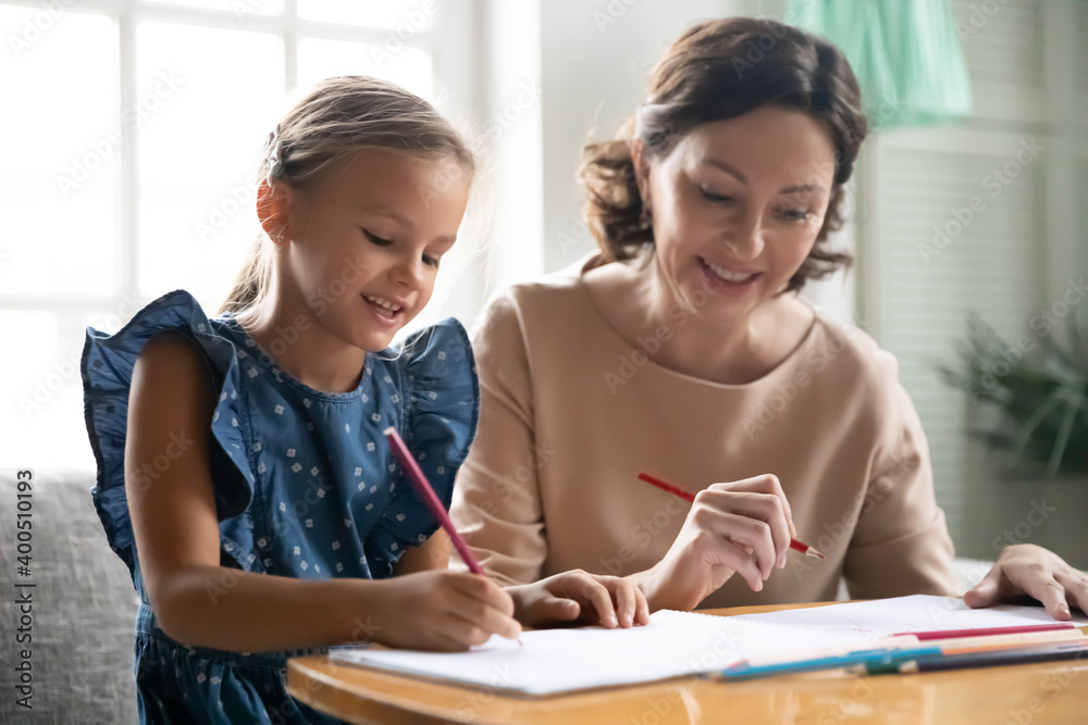 Close up happy middle aged grandmother and little granddaughter drawing pencils, sitting at table, smiling mature woman babysitter teacher and cute girl child engaged in creative activity Close up happy middle aged grandmother and little granddaughter drawing pencils, sitting at table, smiling mature woman babysitter teacher and cute girl child engaged in creative activity