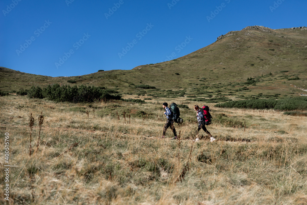 couple in love tourists man and woman stand walking along a mountain path, large backpacks. Hiking concept.