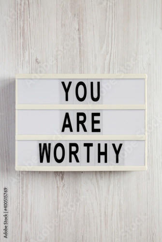 'You are worthy' on a lightbox on a white wooden surface, top view. Flat lay, overhead, from above.