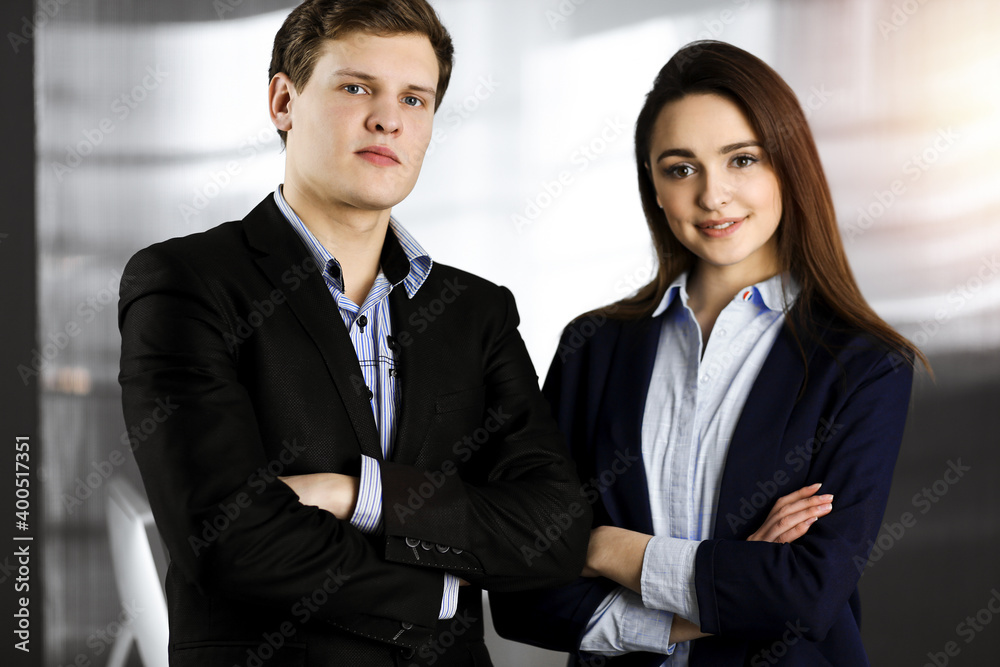 Friendly young colleagues are standing as a team with crossed arms in sunny office. Successful business people at work Friendly young colleagues are standing as a team with crossed arms in sunny office. Successful business people at work