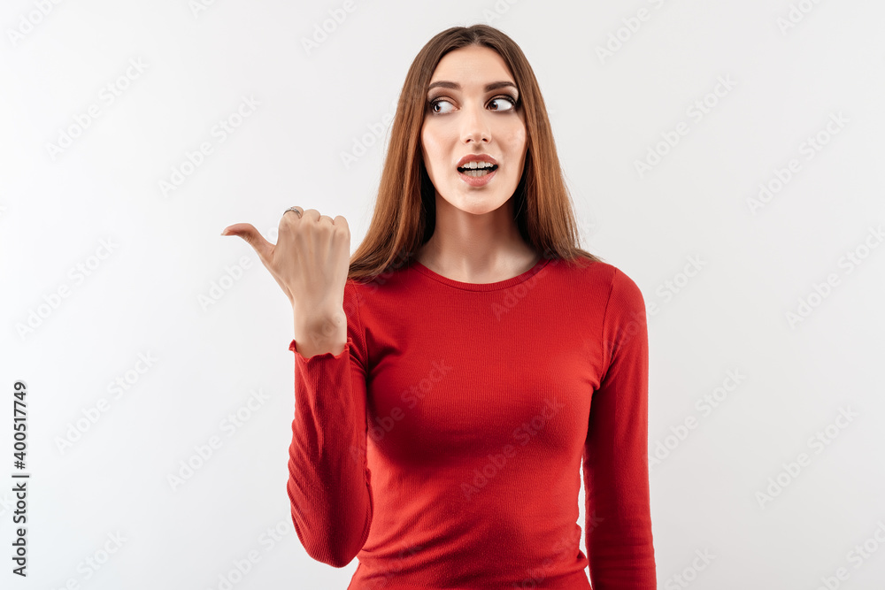Image of young happy woman smiling and pointing thumb aside, shows place for ad Image of young happy woman smiling and pointing thumb aside, shows place for ad