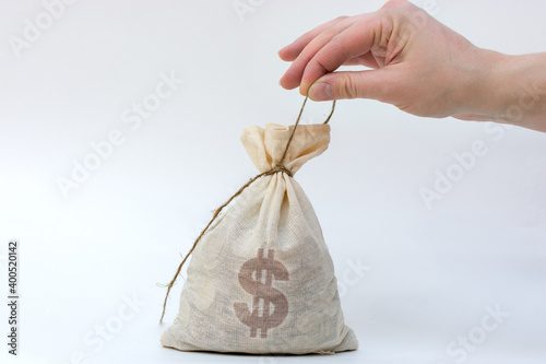 bag with coins on a light background, on the bag a dollar sign. The hand pulls on the rope, trying to untie the bag. Horizontal photo, close-up. photo