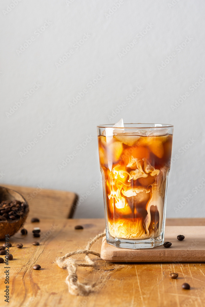 Cold refreshing coffee with ice and creamy clouds in a glass on a wooden board close-up, cocoa beans in coconut shell Cold refreshing coffee with ice and creamy clouds in a glass on a wooden board close-up, cocoa beans in coconut shell