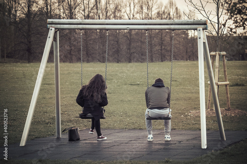 unhappy couple of youths. Back view of two teenagers being in a conflict sitting in a swing in the park