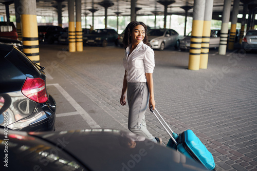 Young woman with suitcase in car parking photo