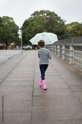 Young girl child holding umbrella at walking along the street during rain