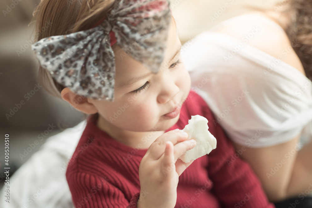 A toddler wearing a red top and a hair band with a hair bow takes a bite of a bun in a house in Edinburgh, Scotland, United Kingdom, with her pinkie sticking up A toddler wearing a red top and a hair band with a hair bow takes a bite of a bun in a house in Edinburgh, Scotland, United Kingdom, with her pinkie sticking up