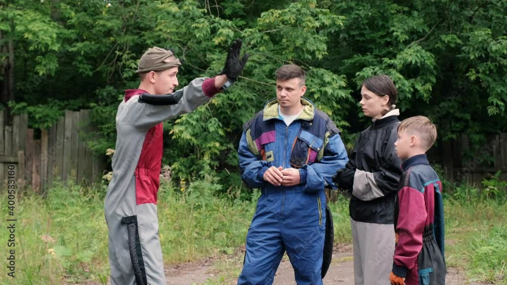 Man instructor gives instructions to the family before the flight in the wind tunnel, aerodynamic tube. They are wearing in special costumes outdoors and listening trainer.