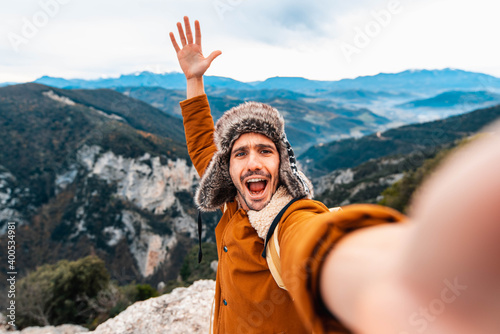 Young man taking a selfie with mobile smart phone hiking mountains - Happy smiling guy looking at camera - Warm autumn filter 