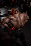Professional black sportsman shows very strong muscular back to the camera. Apartment. Bodybuilding. Sports activity.