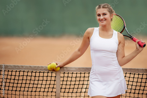 Tennis player. Happy girl, standing with racket and tennis ball on the court, near the net, looking away. Sport concept. © volody10