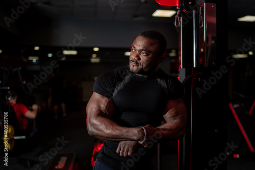 Portrait of young muscular african american man in sport wear looking at side while posing over gym background. Sport, workout, bodybuilding concept.