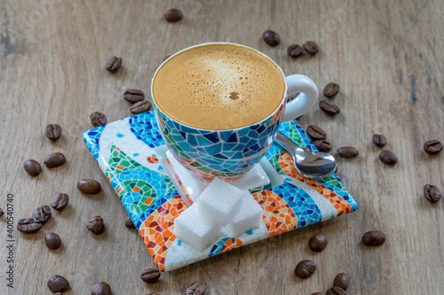 Espresso in Tasse mit Gaudi-Dekor, Löffel, Zuckerwürfel und Kaffeebohnen