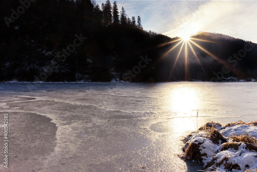 Gefrorener See im Chiemgau mit Eis  Refelxion  Bergen  Wald  und Sonne  Gegenlicht