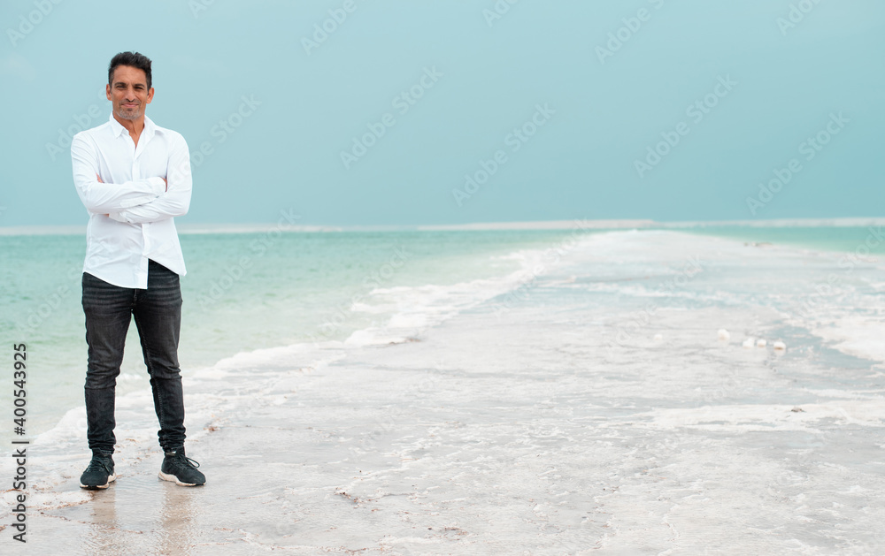 Young businessman stand on the white beach of dead sea. Blue sea paradise for summer holidays. The blue sky merges with endless surfase of the sea. vacation and travel in Israel. Young businessman stand on the white beach of dead sea. Blue sea paradise for summer holidays. The blue sky merges with endless surfase of the sea. vacation and travel in Israel.