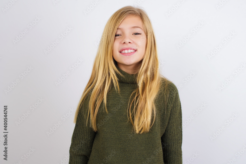 Caucasian kid girl wearing green knitted sweater against white wall with a happy and cool smile on face. Lucky person. Caucasian kid girl wearing green knitted sweater against white wall with a happy and cool smile on face. Lucky person.
