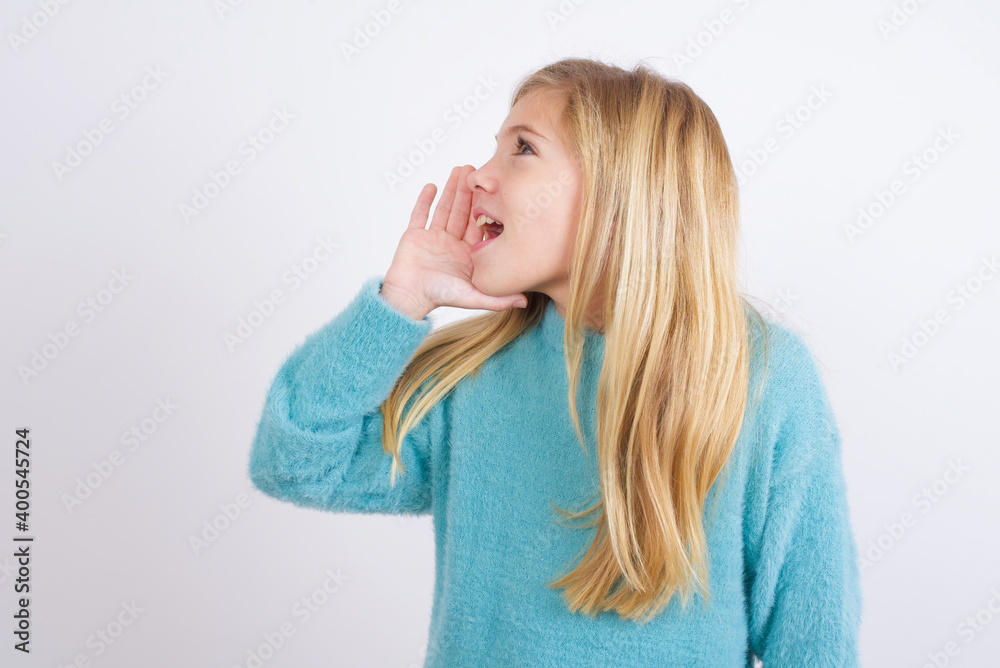 Cute Caucasian kid girl wearing blue knitted sweater against white wall profile view, looking happy and excited, shouting and calling to copy space. Cute Caucasian kid girl wearing blue knitted sweater against white wall profile view, looking happy and excited, shouting and calling to copy space.