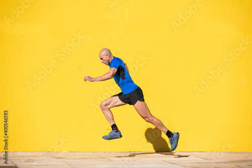 Sportsman starting a big step to run in front of a yellow wall