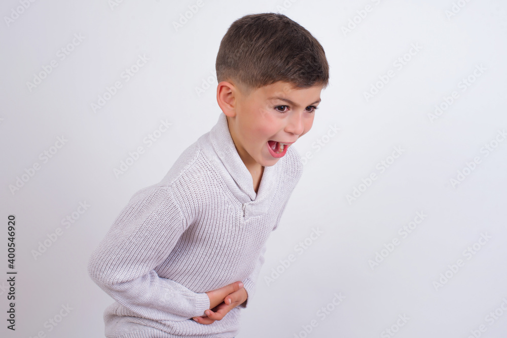 Cute Caucasian kid boy wearing knitted sweater against white wall smiling and laughing hard out loud because funny crazy joke with hands on body. Cute Caucasian kid boy wearing knitted sweater against white wall smiling and laughing hard out loud because funny crazy joke with hands on body.