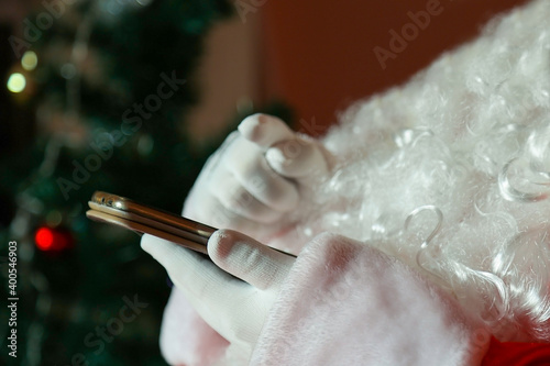 Hands of santa claus in white gloves hold a smartphone.