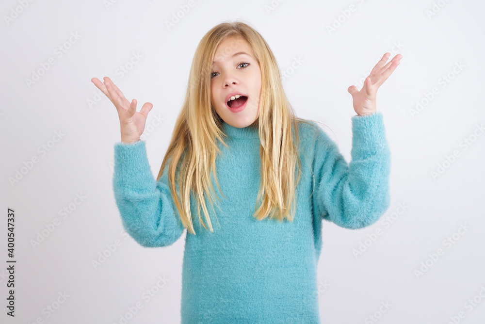 Joyful excited lucky Cute Caucasian kid girl wearing blue knitted sweater against white wall cheering, celebrating success, screaming yes with clenched fists Joyful excited lucky Cute Caucasian kid girl wearing blue knitted sweater against white wall cheering, celebrating success, screaming yes with clenched fists