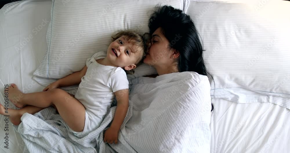 Mother cuddling with baby in morning in bed together, top view Mother cuddling with baby in morning in bed together, top view