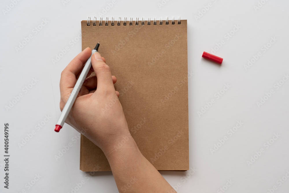 Taking notes in blank craft paper notebook. woman hand and red pencil on white background. isolated. new year's resolution, goals. 2021. coronavirus. lock down, assignment, home office. copy space. Taking notes in blank craft paper notebook. woman hand and red pencil on white background. isolated. new year's resolution, goals. 2021. coronavirus. lock down, assignment, home office. copy space.