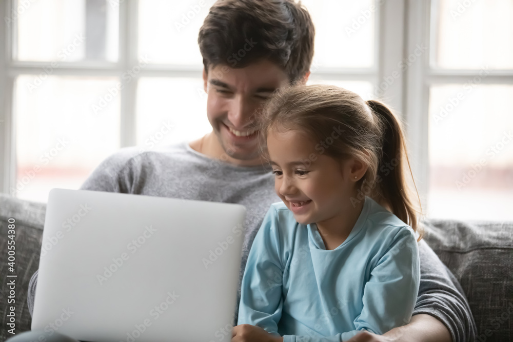 Close up happy father and little daughter using laptop together, sitting on cozy couch at home, smiling dad and adorable preschool girl looking at screen, chatting or shopping online, watching video Close up happy father and little daughter using laptop together, sitting on cozy couch at home, smiling dad and adorable preschool girl looking at screen, chatting or shopping online, watching video