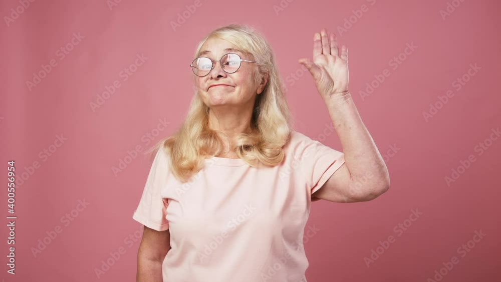 Skeptical elderly woman showing Bla bla gesture with her hand, expressing mistrust and disbelief, pink background