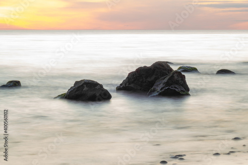 Beautiful sunset over Baltic sea with stones in the water, long exposure photography.