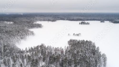 Aerial view of a white snowy lake and land in the winter on a cludy day. Abstract landscape of northern nature.