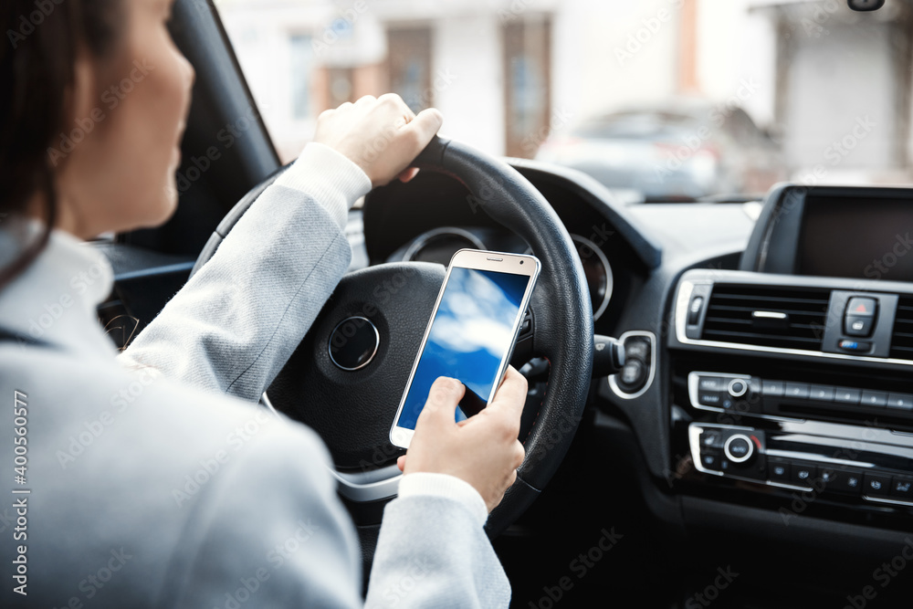 Cropped shot of woman hands holding wheel and smartphone. Businesswoman using mobile phone application while driving, checking route on her way office Cropped shot of woman hands holding wheel and smartphone. Businesswoman using mobile phone application while driving, checking route on her way office