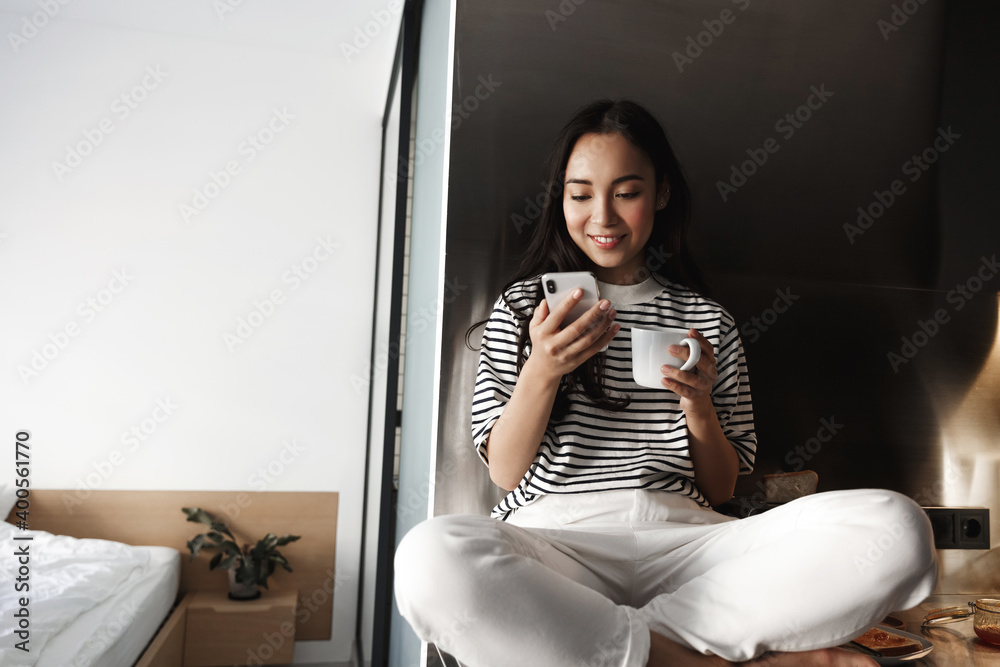 © Liubov Levytska - Lifestyle. Young asian woman sitting at home, resting with coffee and mobile phone, checking social media while relaxing in her bedroom © Liubov Levytska - Lifestyle. Young asian woman sitting at home, resting with coffee and mobile phone, checking social media while relaxing in her bedroom