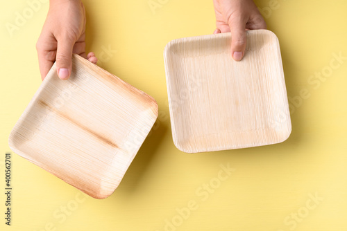 Hand holding betal palm leaf plate (Biodegradable, Compostable, Disposable or Eco friendly plate) on yellow background, Sustainable concept photo