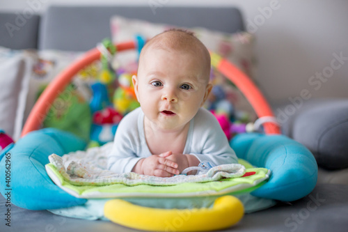 Happy three months old baby boy, playing at home on a colorful activity blanket, toys and different activity