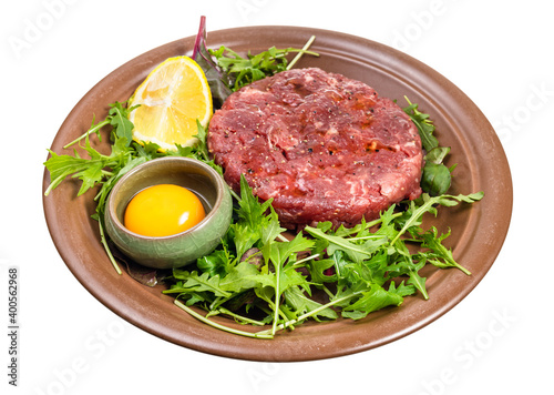 yolk in bowl and Steak tartare (raw minced beef meat ) on fresh greens on brown plate isolated on white background