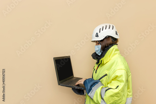 Female industrial worker in medical mask. Woman engineer with white hard hat helmet working on laptop computer. Climber photo