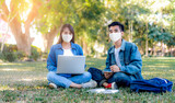 Asian student couple studying together wearing face mask health and safety COVID-19 pandemic, sitting down on the school university campus studying with laptop computer, books, pencil and note book
