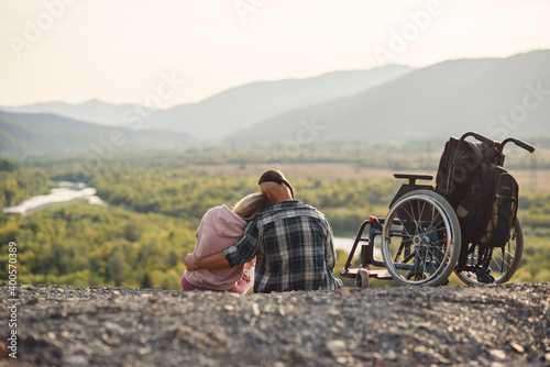 Foto Pretty woman and her incapacitated husband resting together near his wheelchair on the hill