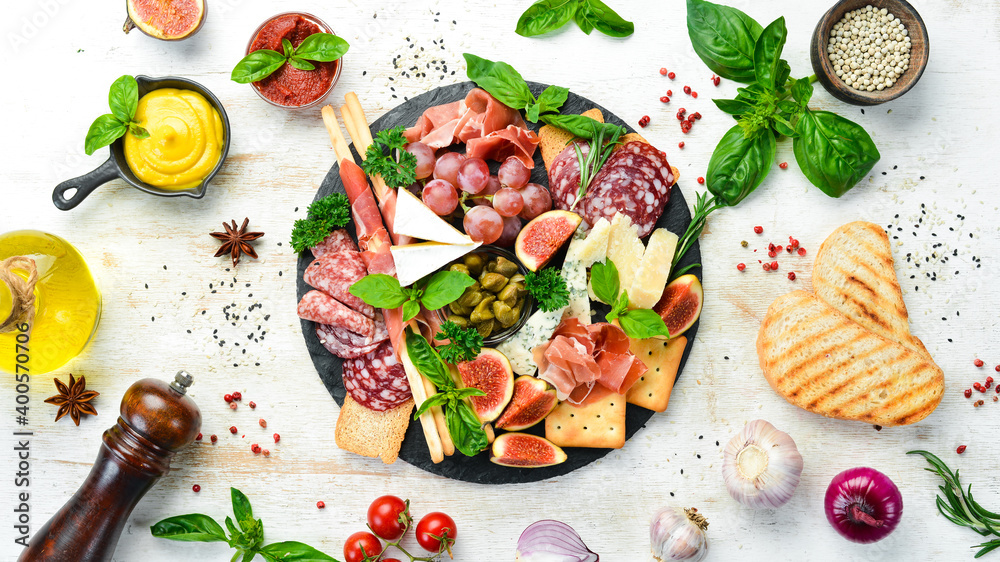 A plate with cheese, salami, prosciutto and snacks on a black stone plate. Antipasto. Top view. Italian food. Free space for your text. A plate with cheese, salami, prosciutto and snacks on a black stone plate. Antipasto. Top view. Italian food. Free space for your text.