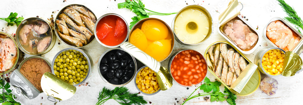 Food background in tin cans. Canned vegetables, beans, fish and fruits on a white wooden background. Top view. Food background in tin cans. Canned vegetables, beans, fish and fruits on a white wooden background. Top view.