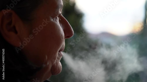 Woman smoking a cigar outdoors in the field and releasing the smoke through her nose and mouth. Woman relaxing smoking a cigarette outdoors at sunset.