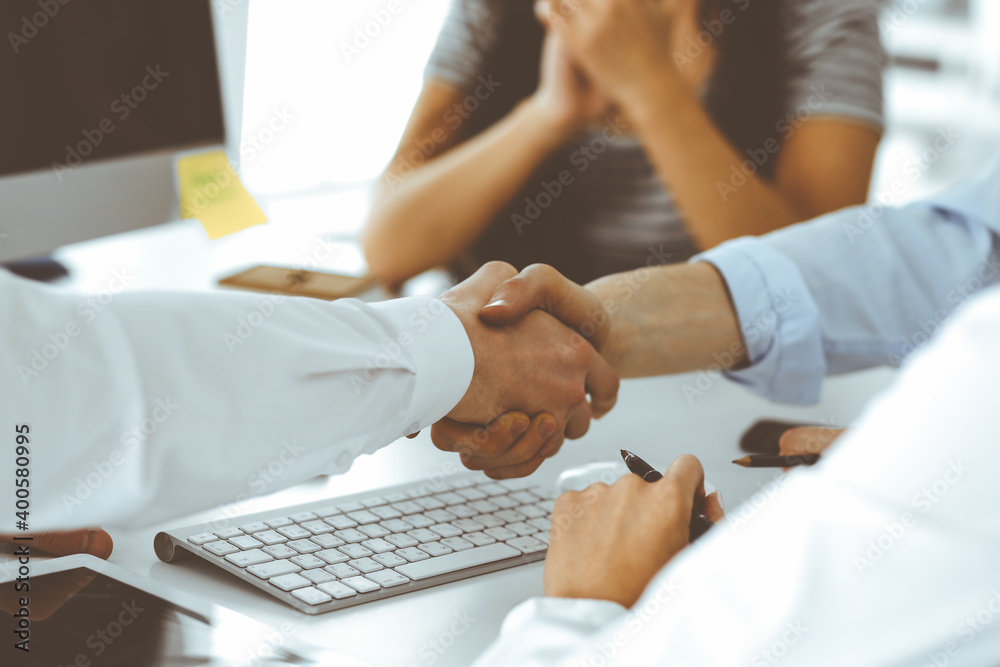 Two businessmen are shaking hands in office while sitting at the desk, close-up. Colleagues applauding of success meeting end. Business people concept Two businessmen are shaking hands in office while sitting at the desk, close-up. Colleagues applauding of success meeting end. Business people concept