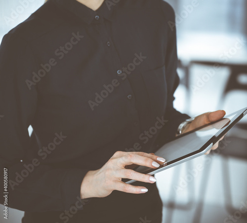 Unknown business woman using tablet computer while standing straight in office, close-up. Data in business