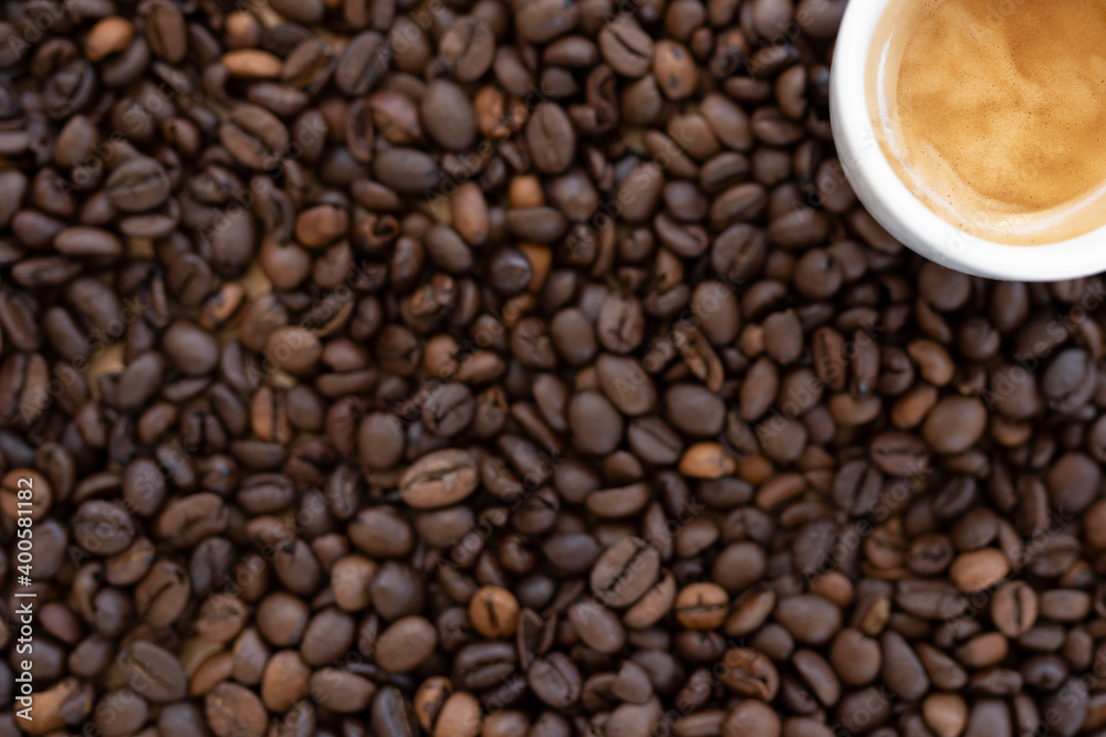Flat lay with copy space, (selective focus) A white espresso cup with some creamy coffee is placed on some blurred roasted coffee beans. Flat lay with copy space, (selective focus) A white espresso cup with some creamy coffee is placed on some blurred roasted coffee beans.